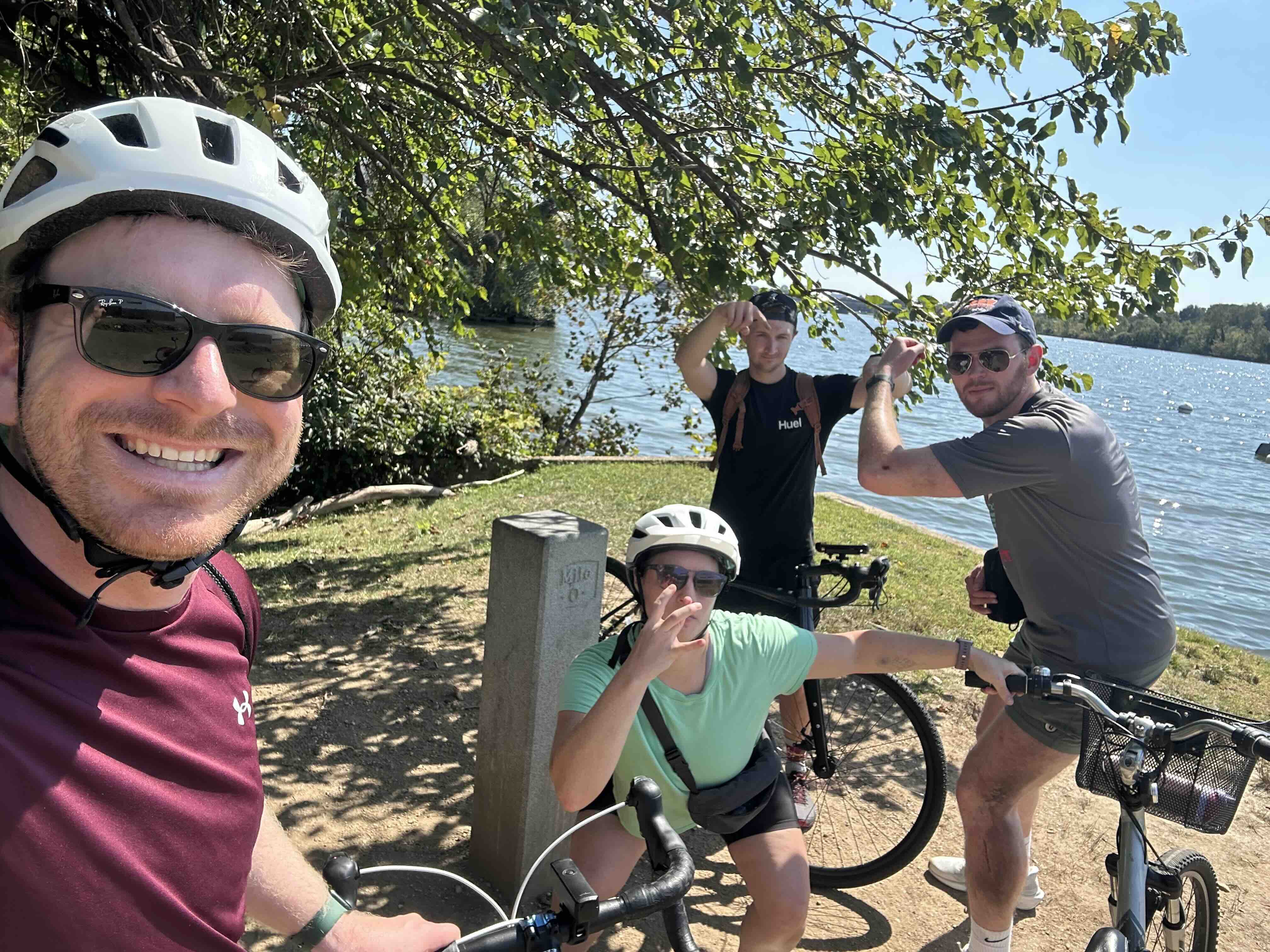 Four cyclists posing with their bikes beside the Mile Zero marker